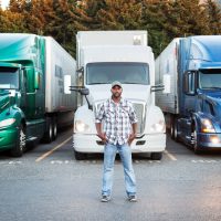 Black man truck driver near his truck parked in a parking lot at a truck stop